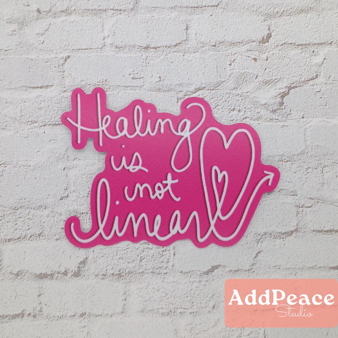 Pink sign with 'Healing is not linear' text on a textured white background, featuring the AddPeace Studios logo.
